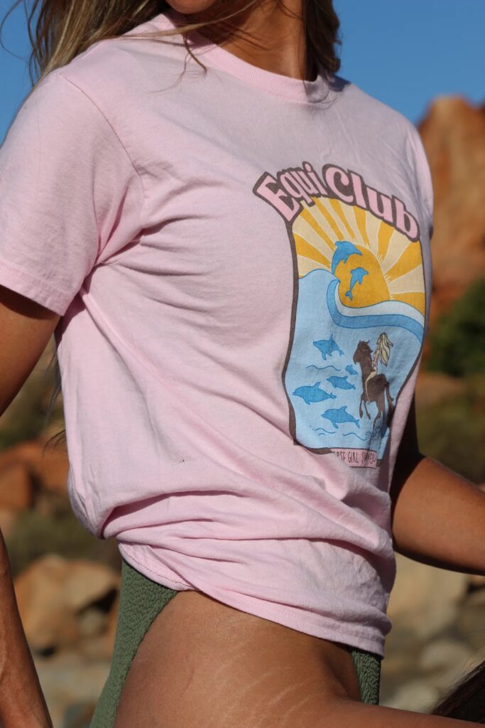 Girl riding horse bareback on a beach in a swimsuit and horse girl tee. Equiclub is an equestrian apparel brand made for ocean, beach loving horse girls. 